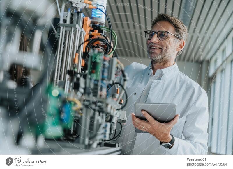 Lächelnder männlicher Wissenschaftler hält digitale Tablett-Untersuchungsmaschine im Labor Farbaufnahme Farbe Farbfoto Farbphoto Innenaufnahme Innenaufnahmen