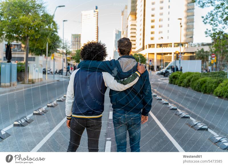 Rückansicht von zwei sich umarmenden Männern auf der Straße in der Stadt, Barcelona, Spanien Leute Menschen People Person Personen Europäisch Kaukasier