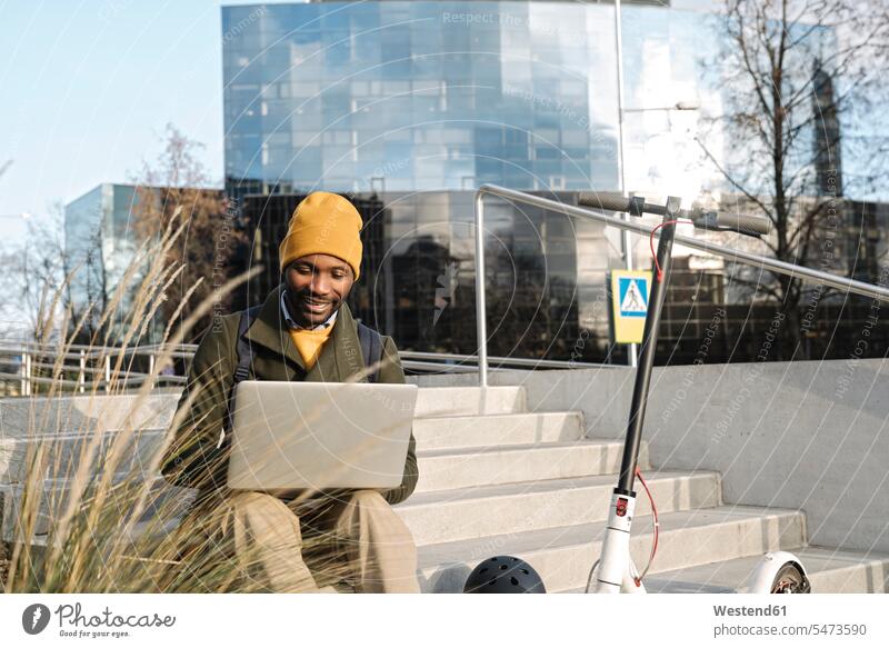 Stilvoller Mann mit Laptop vor dem Büro mit einem Roller neben sich Job Berufe Berufstätigkeit Beschäftigung Jobs geschäftlich Geschäftsleben Geschäftswelt