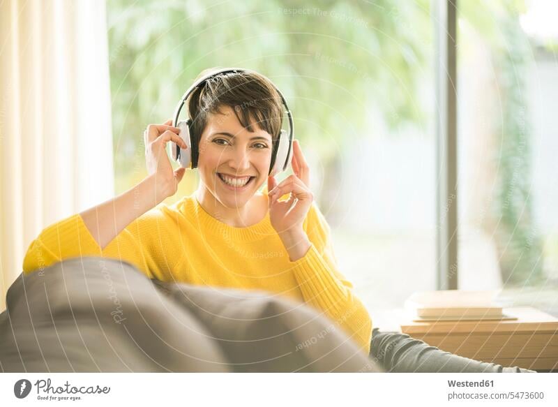 Porträt der glücklichen Frau sitzt auf der Couch zu Hause hören Musik mit Kopfhörern Portrait Porträts Portraits weiblich Frauen Glück glücklich sein