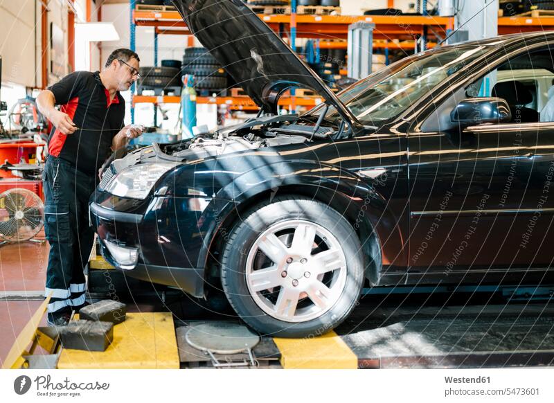 Männlicher Mechaniker repariert Auto, während er in einer Autowerkstatt steht Farbaufnahme Farbe Farbfoto Farbphoto Spanien Innenaufnahme Innenaufnahmen innen