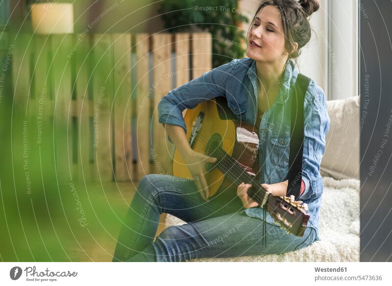 Passionierte Frau spielt Gitarre zu Hause sitzen sitzend sitzt weiblich Frauen spielen Gitarren Zuhause daheim Leidenschaft leidenschaftlich