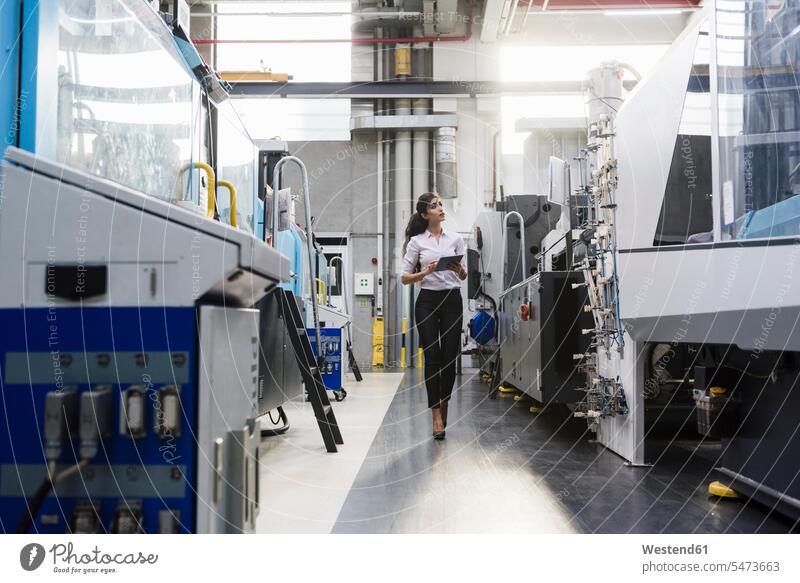 Frau mit Tablet an Maschine in Fabrikhalle schaut sich um Industriehallen Fabrikhallen Maschinen Fabriken umherblicken umschauen umsehen Tablet Computer