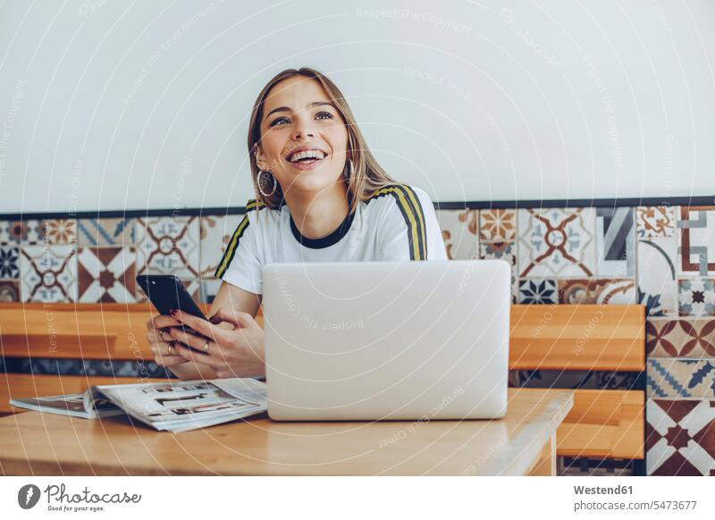 Junge Frau benutzt das Mobiltelefon und den Laptop im Café Information Zeitschrift Handy halten lernen lächeln sitzen studieren Freude glücklich Zufriedenheit