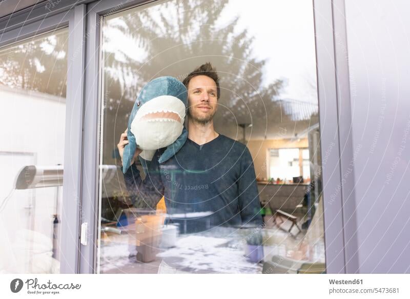 Mann schaut aus dem Fenster, trägt Spielzeug-Hai auf der Schulter stehen stehend steht Kuscheltier Kuscheltiere Haie Haifisch Haifische Glasscheibe Glasscheiben