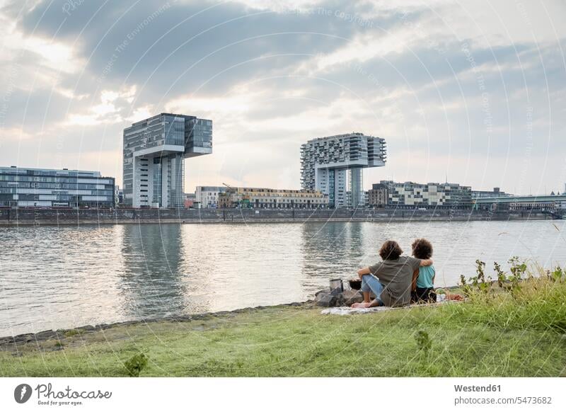 Deutschland, Köln, Paar entspannt am Flussufer bei Sonnenuntergang entspanntheit relaxt Pärchen Paare Partnerschaft Sonnenuntergänge Entspannung relaxen