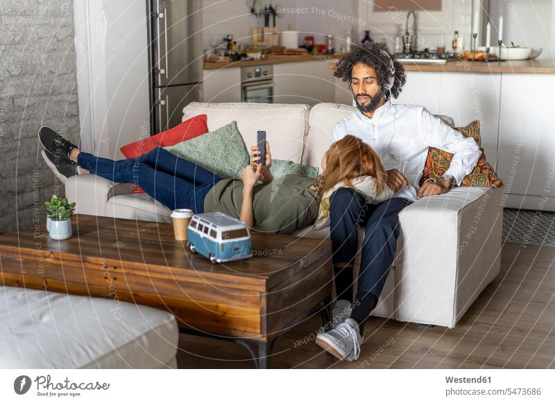 Paar entspannt sich auf der Couch und plant ihren Roadtrip Sofa Couches Liege Sofas Zuhause zu Hause daheim Musik hören Urlaub Ferien Autoreise Smartphone