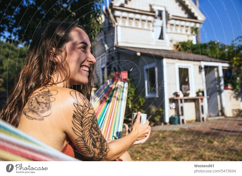 Glückliche junge Frau mit Tätowierung in Hängematte glücklich glücklich sein glücklichsein weiblich Frauen Hängematten Tattoo Tätowierungen Tatoos Taetowierung