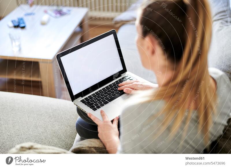 Hochwinkelansicht einer Frau, die einen Laptop benutzt, während sie zu Hause auf dem Sofa sitzt Farbaufnahme Farbe Farbfoto Farbphoto Deutschland