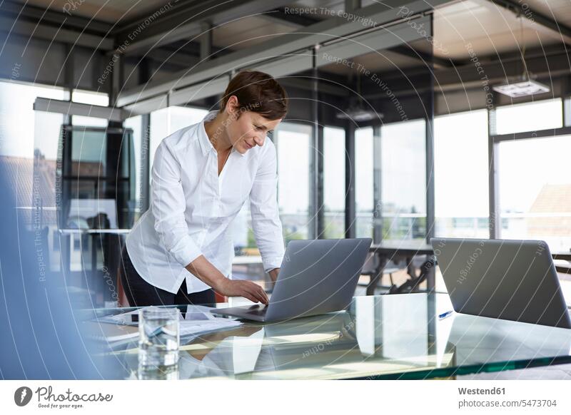 Geschäftsfrau, die im Büro am Glastisch steht und einen Laptop benutzt stehen stehend Geschäftsfrauen Businesswomen Businessfrauen Businesswoman Office Büros