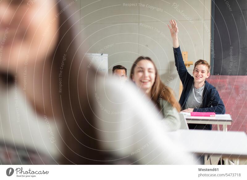 Lächelnder Teenager hebt die Hand in der Klasse melden sich melden Schule Schulen Jugendliche Heranwachsende Pubertierende Schulklasse Klassenzimmer Klassenraum