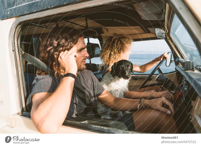 Junge Frau sitzt bei Hund und Mann, während sie am Strand Auto fährt Tiermotive Tierthemen Tiere Tierwelt Freizeitkleidung Freizeitbekleidung casual