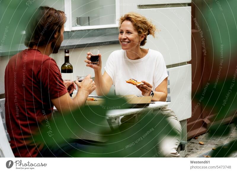 Glückliches Paar sitzt im Garten, isst Pizza, trinkt Wein Gärten Gaerten Rotwein Rotweine glücklich glücklich sein glücklichsein essen essend Pärchen Paare