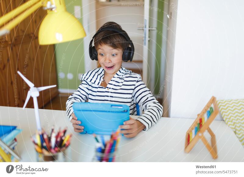 Junge macht Heimunterricht und benutzt Tablet und Kopfhörer zu Hause Windräder Windturbine Windturbinen Tische Arbeitstisch Schreibtische Kopfhoerer hoeren