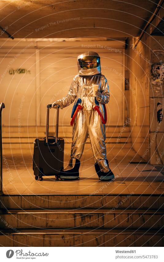Raumfahrer in der Stadt bei Nacht in Unterführung stehend mit Rollkoffer und Kaffee zum Mitnehmen Astronaut Astronauten nachts Unterführungen staedtisch