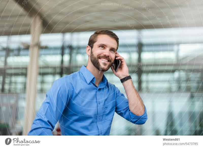 Lächelnder junger Geschäftsmann am Handy im Freien lächeln wegsehen Blick zur Seite wegschauen telefonieren anrufen Anruf telephonieren Businessmann
