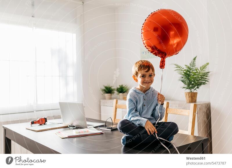 Junge sitzt auf dem Esstisch mit einem roten Luftballon in der Hand sitzen sitzend Luftballons Ballons Luftballone Ganzkörperansicht Ganzansicht