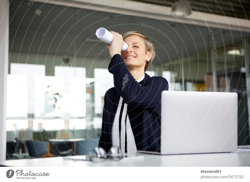 Lächelnde Geschäftsfrau blickt am Schreibtisch im Büro durch Papierrollen Job Berufe Berufstätigkeit Beschäftigung Jobs geschäftlich Geschäftsleben