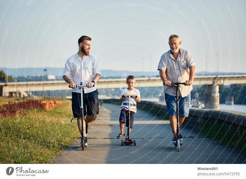 Großvater, Vater und Sohn fahren Roller am Flussufer Leute Menschen People Person Personen Europäisch Kaukasier kaukasisch Gruppe von Menschen Menschengruppe