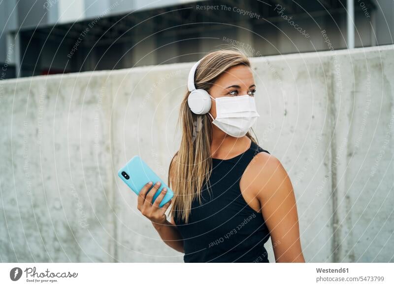 Junge sportliche Frau mit Schutzmaske, Kopfhörer und Smartphone Kopfhoerer Telekommunikation telefonieren Handies Handys Mobiltelefon Mobiltelefone hoeren Muße
