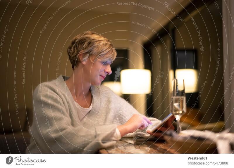 Blonde Frau arbeitet spät, während sie ein digitales Tablet im beleuchteten Wohnzimmer benutzt Farbaufnahme Farbe Farbfoto Farbphoto Deutschland Tablet-Computer