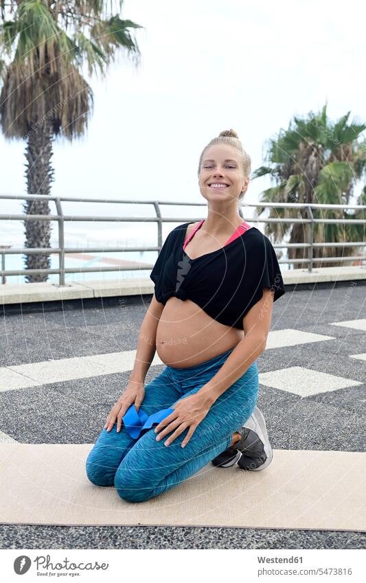 Porträt der lächelnden schwangeren Frau kniend auf Gymnastikmatte im Freien Schwangere schwangere Frau weiblich Frauen Portrait Porträts Portraits