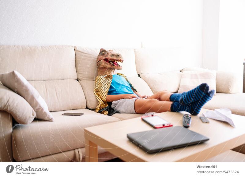 Junge mit Dinosaurier-Maske entspannt sich zu Hause auf dem Sofa Farbaufnahme Farbe Farbfoto Farbphoto Spanien Innenaufnahme Innenaufnahmen innen drinnen