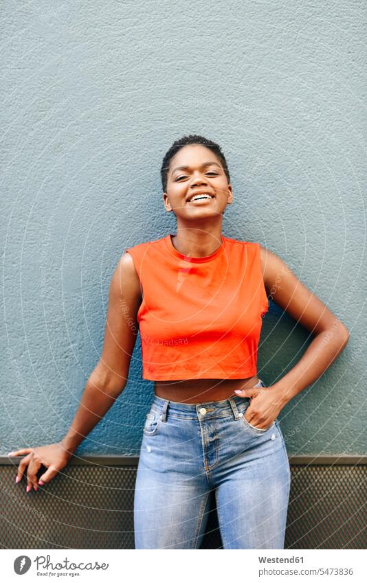 Porträt einer lächelnden jungen Frau, die an der Wand lehnt Hosen Jeanshose freuen zufrieden stehend steht Muße Lifestyles Attraktivität gut aussehend