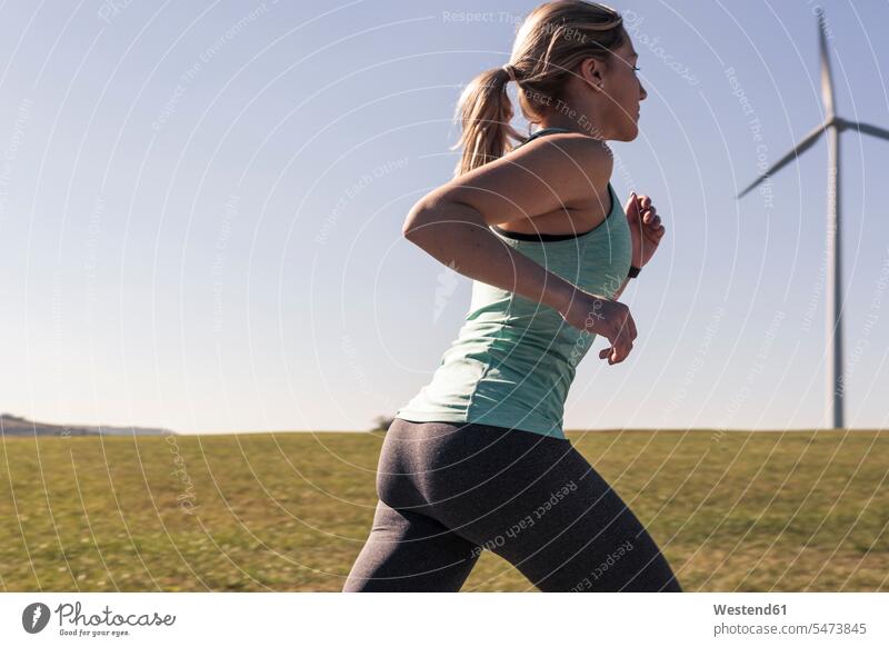 Junge Frau joggt auf Feldweg, Windräder im Hintergrund Windrad Windturbinen Feldwege umweltfreundlich ökofreundlich Joggerin Joggerinnen weiblich Frauen Joggen