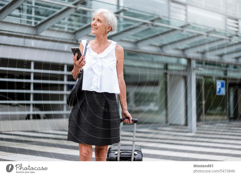 Lächelnde Seniorin mit Mobiltelefon und Gepäck unterwegs älter Seniorinnen alt Frau weiblich Frauen Reisegepäck Handy Handies Handys Mobiltelefone lächeln