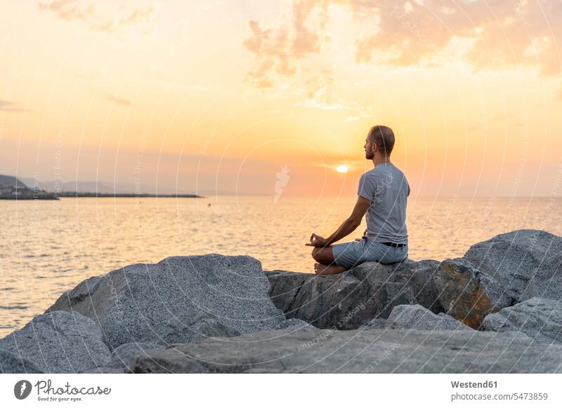 Spanien: Mann meditiert bei Sonnenaufgang an felsigem Strand Fels Felsen meditieren Yoga Yoga-Übungen Yogauebungen Yogaübungen Jogauebung Jogauebungen