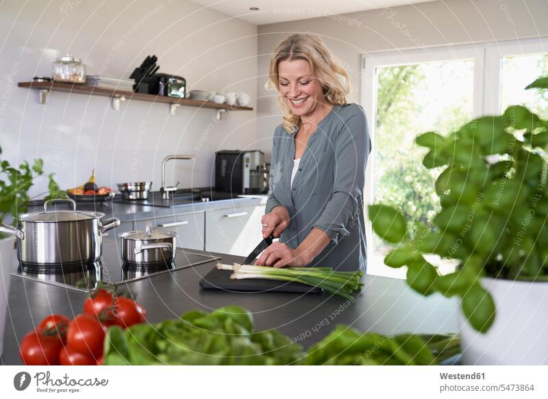 Lächelnde Frau schneidet Frühlingszwiebeln in der Küche Küchen Lauchzwiebel Lauchzwiebeln weiblich Frauen schneiden lächeln Gemüse Gemuese Essen Food