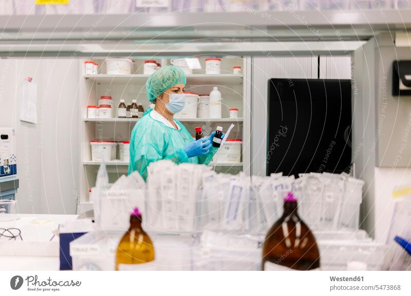 Apothekerin hält Flaschen in der Hand, während sie im Krankenhaus am Regal steht Farbaufnahme Farbe Farbfoto Farbphoto Spanien Innenaufnahme Innenaufnahmen