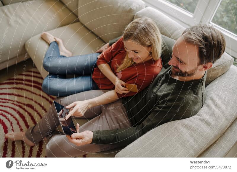 Paar, das zu Hause auf der Couch sitzt und ein digitales Tablet benutzt Leute Menschen People Person Personen Europäisch Kaukasier kaukasisch 2 2 Menschen