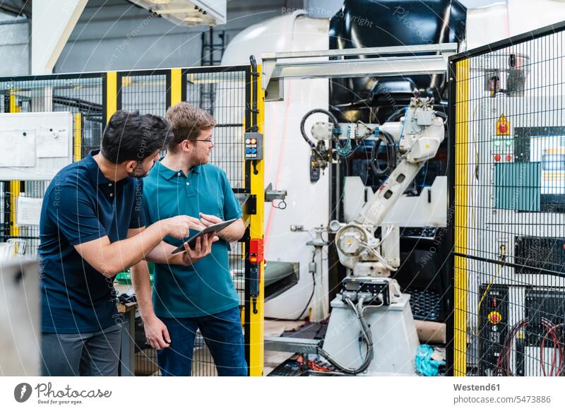 Männliche Mitarbeiter halten ein digitales Tablet und schauen auf einen Roboterarm, während sie in der Fertigungsindustrie stehen Farbaufnahme Farbe Farbfoto