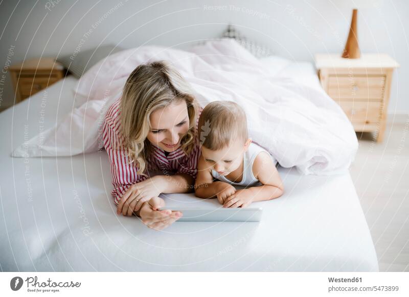 Lächelnde Mutter und Kleinkind Sohn liegen im Bett zu Hause mit Tablette Mami Mutti Mütter Mama Söhne Zuhause daheim Tablet Computer Tablet-PC Tablet PC iPad