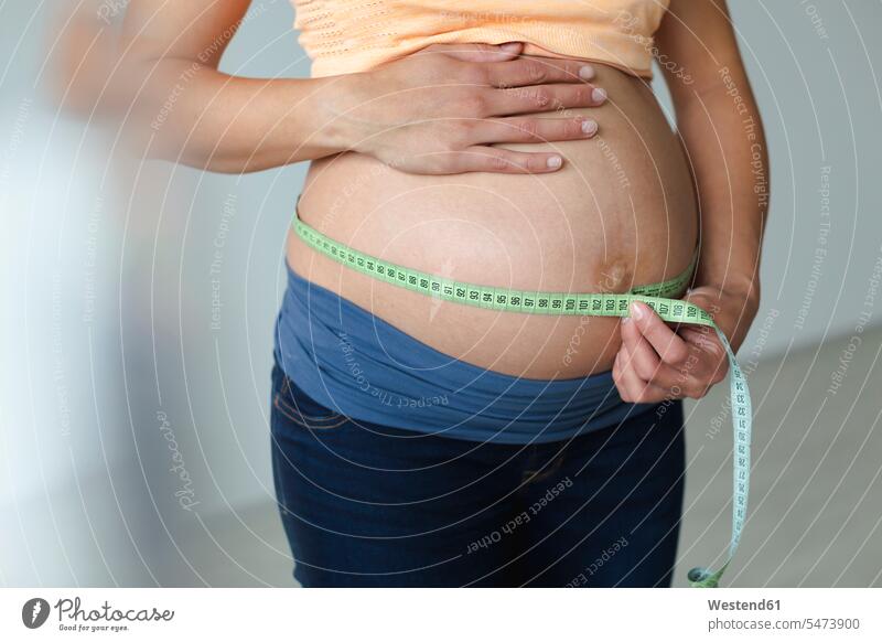 Junge schwangere Frau, die ihren Babybauch misst Massband Messband Metermaß Glück glücklich sein glücklichsein daheim zu Hause Schwangere entwickeln