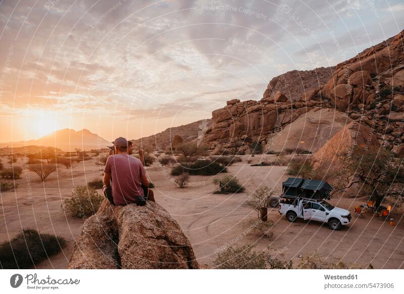Namibia, Spitzkoppe, Freunde sitzen auf einem Felsen und beobachten den Sonnenuntergang Sonnenuntergänge zusehen zusehend sitzend sitzt Stimmung stimmungsvoll
