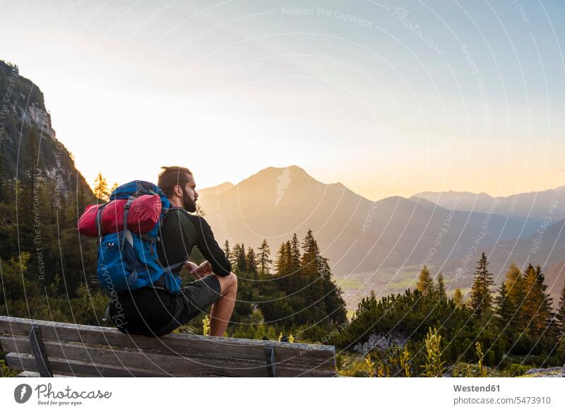 Österreich, Tirol, Wanderer in der Pause, auf der Bank sitzend, auf die Aussicht schauend Holzbank Holzbänke Holzbaenke Pause machen Sonnenuntergang