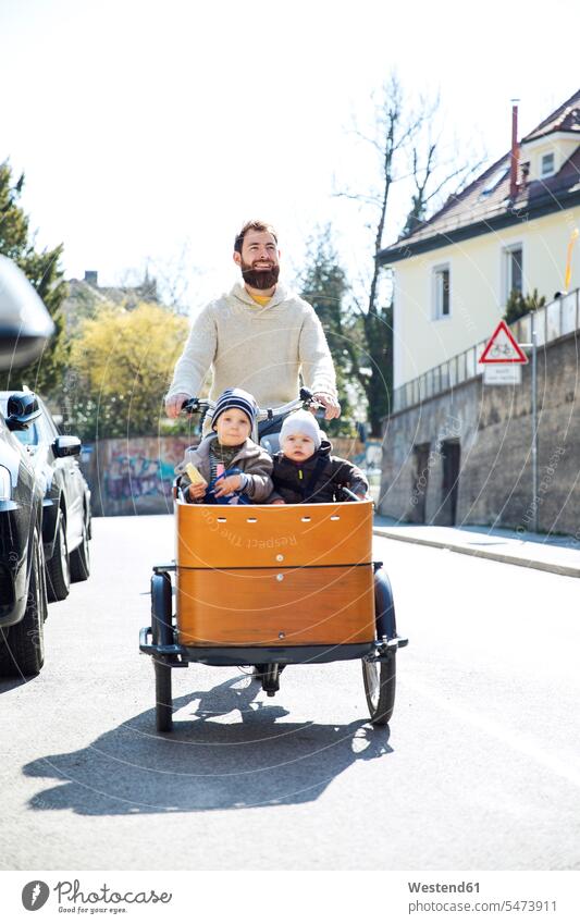 Glücklicher Vater mit zwei Kindern fahren Cargo Fahrrad in der Stadt Papas Väter Vati Vatis Papis Lastenfahrrad staedtisch städtisch Babies Babys glücklich