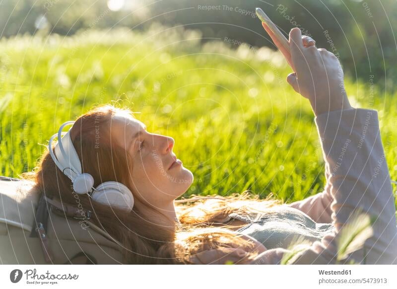 Junge rothaarige Frau mit Kopfhörer und Smartphone in einem Park Kopfhoerer Telekommunikation telefonieren Handies Handys Mobiltelefon Mobiltelefone entspannen