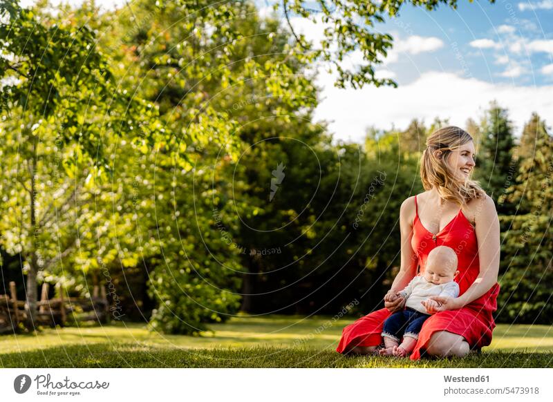 Lächelnde Mutter hält Baby Junge, während kniend auf grasigen Land im Park Farbaufnahme Farbe Farbfoto Farbphoto Kanada Canada Freizeitbeschäftigung Muße Zeit