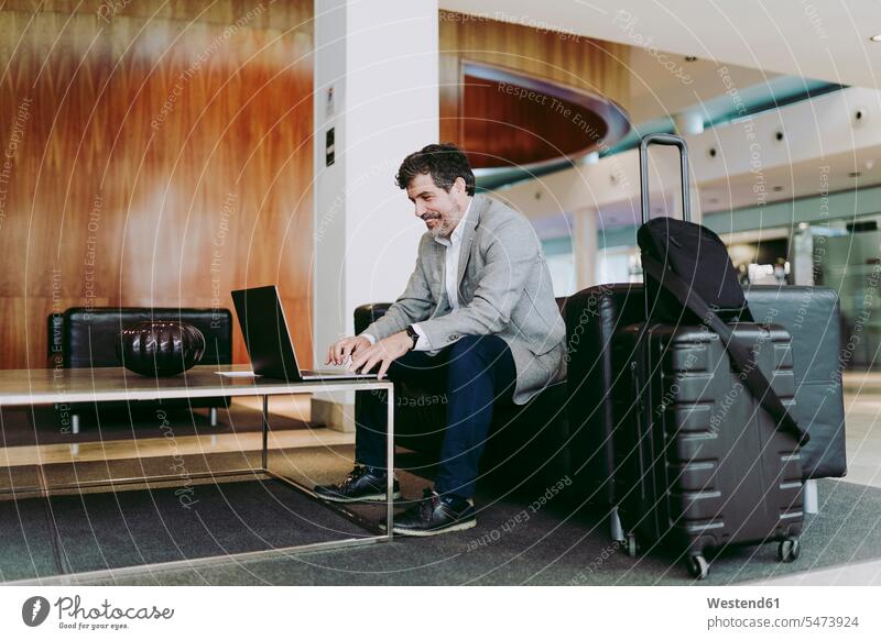 Ein reifer Geschäftsmann benutzt einen Laptop, während er in der Hotellobby sitzt Farbaufnahme Farbe Farbfoto Farbphoto Innenaufnahme Innenaufnahmen innen