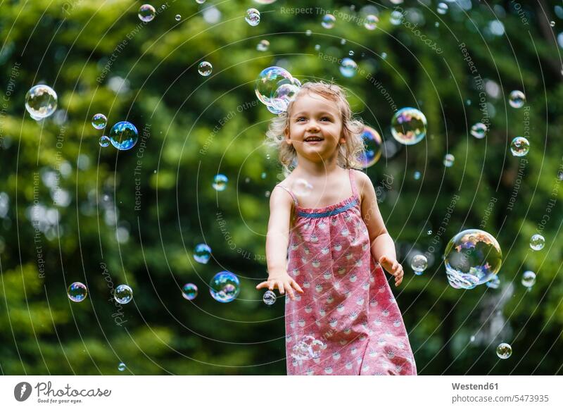Glückliches Mädchen genießt beim Laufen inmitten von Blasen im Park Farbaufnahme Farbe Farbfoto Farbphoto Außenaufnahme außen draußen im Freien Tag