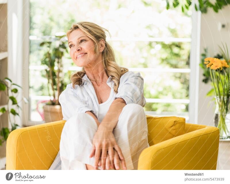 Porträt einer lächelnden reifen Frau, die sich zu Hause im Sessel entspannt entspannen relaxen sitzend sitzt freuen Glück glücklich sein glücklichsein Farben