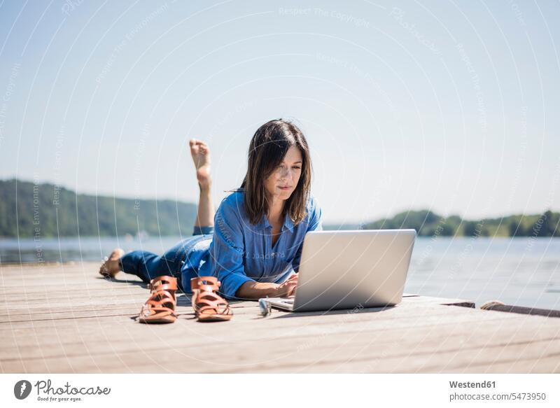 Reife Frau arbeitet an einem See, mit Laptop auf einem Steg Laptop benutzen Laptop benützen arbeiten Arbeit Notebook Laptops Notebooks Seen Sommer Sommerzeit