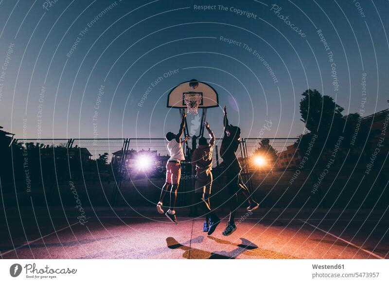 Männliche afrikanische Freunde spielen nachts vor Gericht Basketball gegen den klaren Himmel Farbaufnahme Farbe Farbfoto Farbphoto Spanien Freizeitbeschäftigung