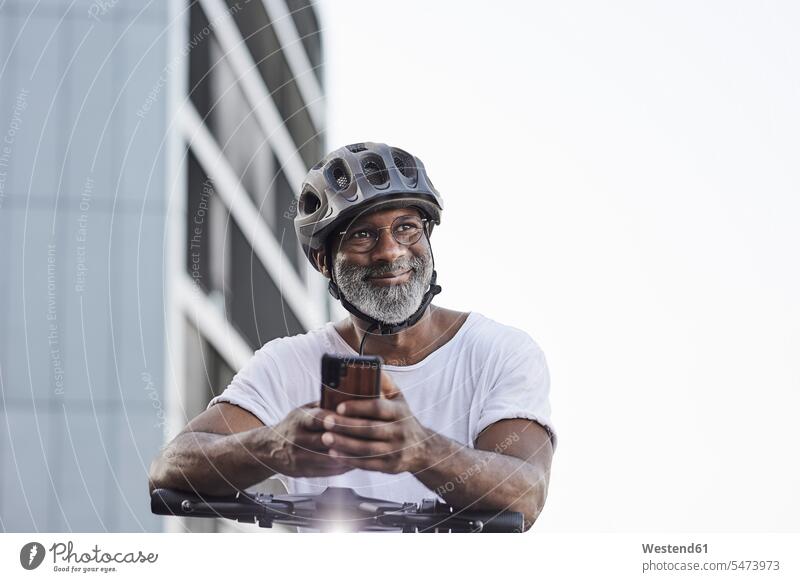 Porträt eines glücklichen reifen Mannes mit Fahrradhelm, der sich auf den Lenker eines Elektrorollers stützt T-Shirts Telekommunikation Handies Handys