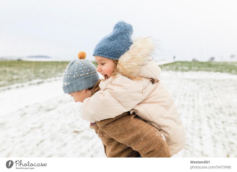 Junge trägt glückliche Schwester Huckepack in Winterlandschaft Bruder Brüder Schwestern tragen transportieren winterlich Winterzeit Glück glücklich sein