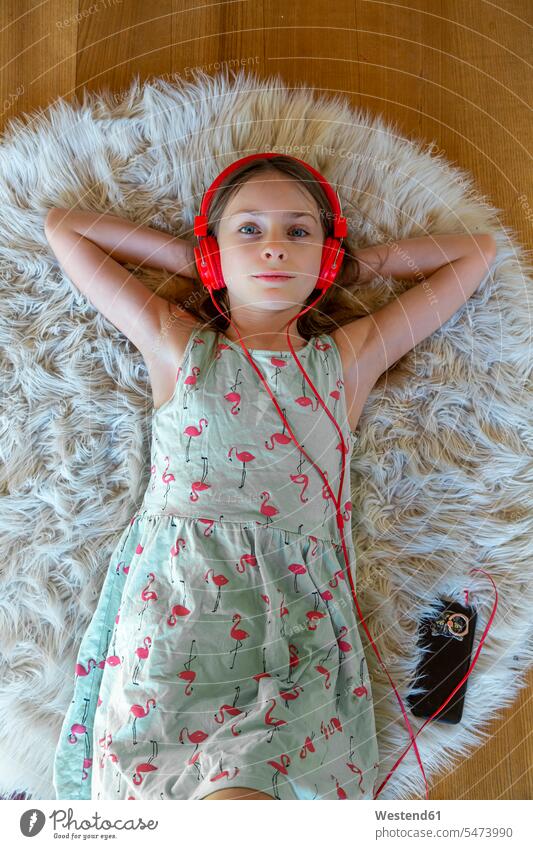 Mädchen liegend auf Teppich zu Hause Musik hören mit Kopfhörer und Smartphone Deutschland Hand hinter dem Kopf Hände hinter dem Kopf Haende hinter dem Kopf
